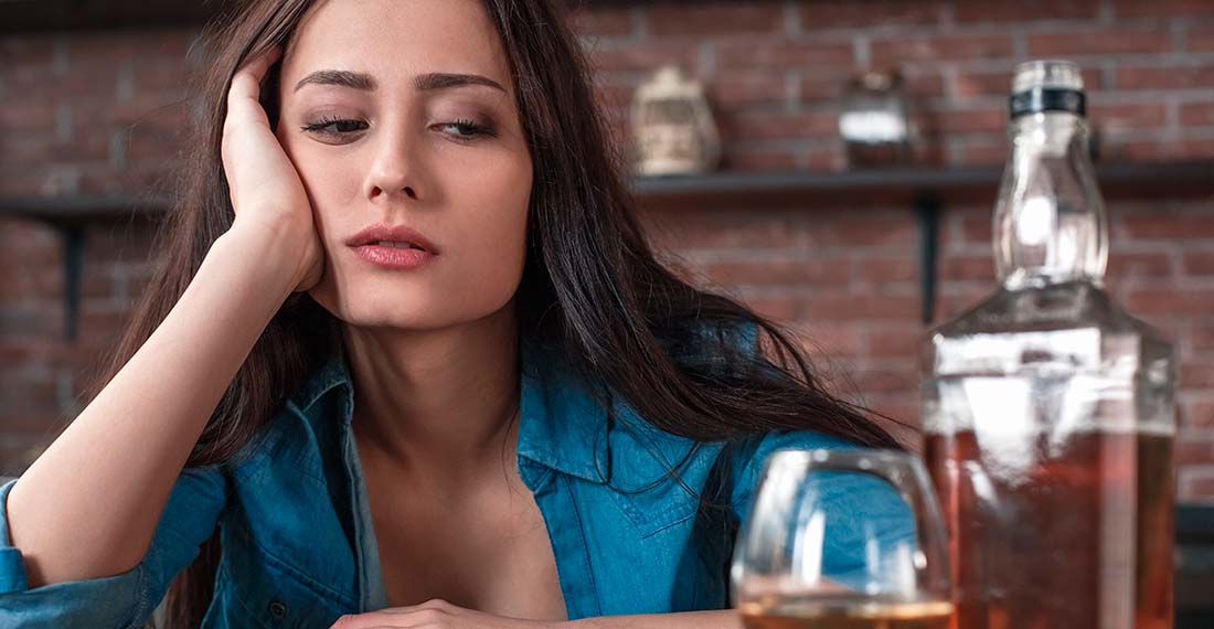 девушка с усталостью смотрит на бутылку с алкоголем